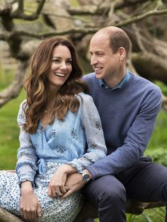 a man and woman are sitting on a tree branch smiling at each other while looking into the distance