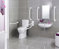 a white toilet sitting next to a sink in a bathroom with gray tiled walls and floor