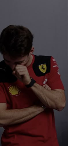 a man in a red shirt is holding his hand to his face and looking down