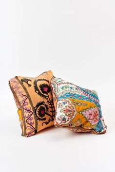 two decorative pillows sitting side by side on a white surface, one is orange and the other is pink