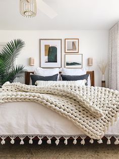 a large white blanket on top of a bed next to two framed pictures and a potted plant