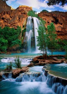 the waterfall is surrounded by green trees and rocks, with blue water running down it