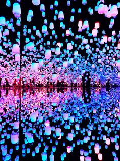 many lit up lanterns floating in the air above water at night time with reflections on the surface