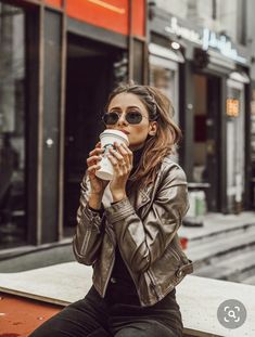 a woman sitting on the curb drinking from a coffee cup