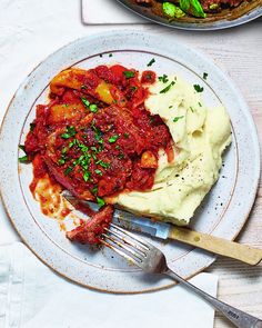 a plate with mashed potatoes, meat and sauce on it next to a skillet