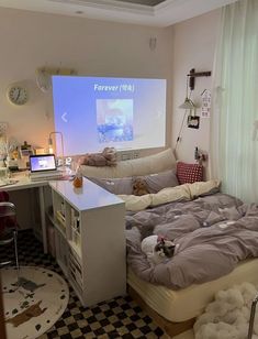 a room with a bed, desk and projection screen on the wall in it's corner