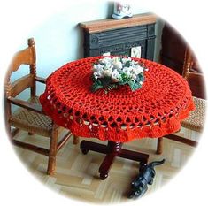 a red crocheted tablecloth with flowers on it sits in front of a fireplace