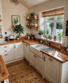 a kitchen with white cabinets and wooden counter tops, plants on the window sill