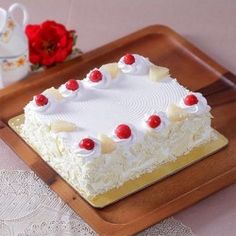 a white cake with cherries on it sitting on a wooden tray next to a cup and saucer