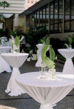 tables with white tablecloths and green plants in vases on the side walk