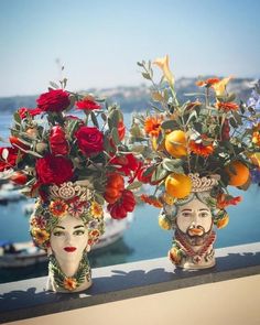 two vases filled with flowers and fruit on top of a ledge next to water