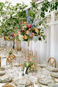 the table is set with plates and flowers in tall vases, along with place settings