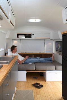 a man sitting on a couch inside of a camper with wood flooring and white walls