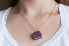 a woman wearing a necklace with a book pendant on it's neck, in front of a white shirt