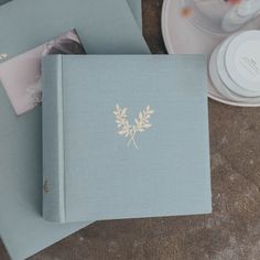 two blue books sitting next to each other on top of a wooden table with plates and cups