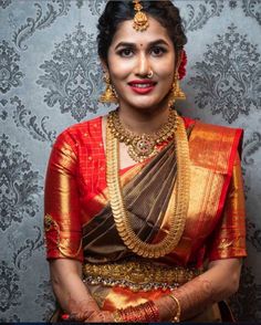 a woman in a red and gold sari with her hands on her hips, smiling at the camera