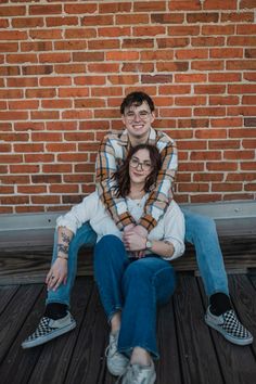 a man and woman sitting next to each other on a wooden floor in front of a brick wall