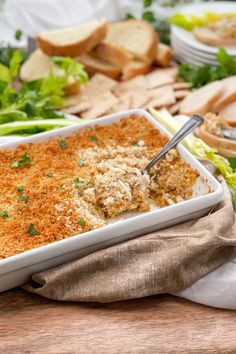 a white casserole dish filled with meat and vegetables on a wooden cutting board