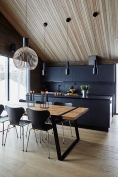 a dining room table surrounded by chairs in front of an open kitchen with wooden ceiling