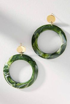 two circular earrings with green and white designs on the front, one in gold plated metal