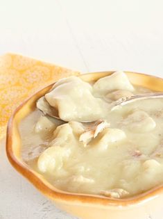 a yellow bowl filled with dumplings on top of a white table next to a spoon