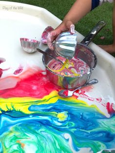 a child is painting on the table with colorful paint and spoons in it,