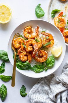 shrimp and rice with lemon wedges on a white plate next to a bowl of spinach