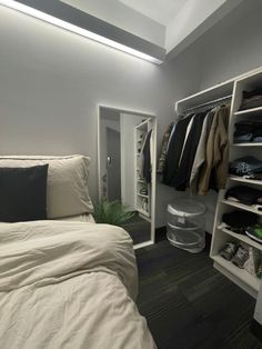 a white bed sitting under a window next to a closet filled with clothes and other items