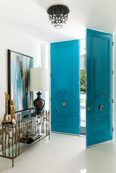 two blue doors in a white room with a chandelier on the wall and an art piece