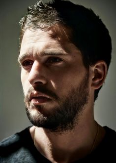 a close up of a person with a beard and wearing a black t - shirt