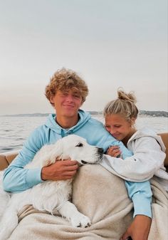 a man and woman are sitting on a boat with their dog, who is wrapped in a blanket