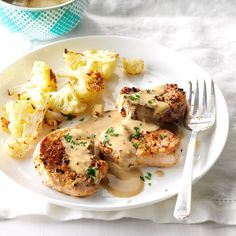 a white plate topped with meat covered in gravy next to cauliflower