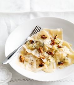 a white plate topped with pasta covered in sauce and nuts next to a silver fork