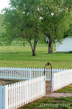 a white picket fence in the middle of a grassy field next to a small house