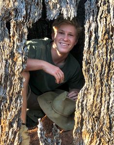 a young man wearing a green hat sitting in a tree