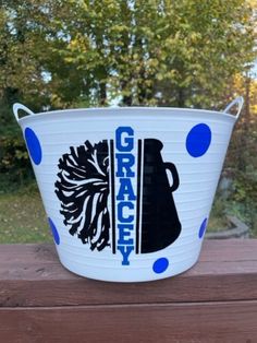 a white bucket sitting on top of a wooden table in front of some trees with blue dots