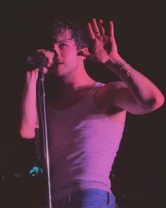 a male in a white shirt is holding his hands up to the air while singing into a microphone