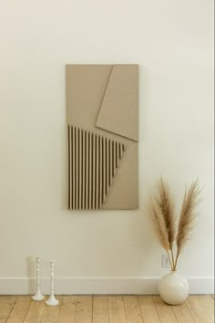 a white vase with some dry grass in it next to a painting on the wall