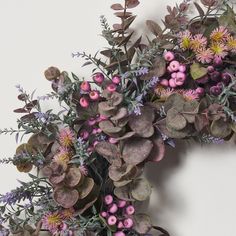 an arrangement of purple flowers and greenery against a white wall