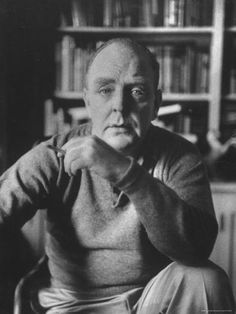 an old man sitting in front of a book shelf with his hand on his chin