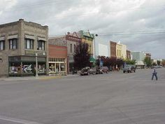 an empty street with cars parked on the side and people walking down the road in front