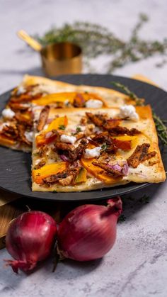 two slices of pizza sitting on top of a black plate next to onions and herbs