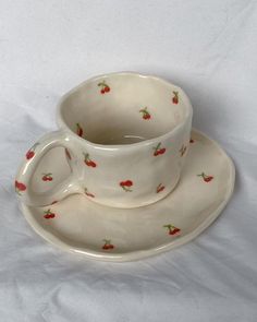 a white cup and saucer with red cherries on it