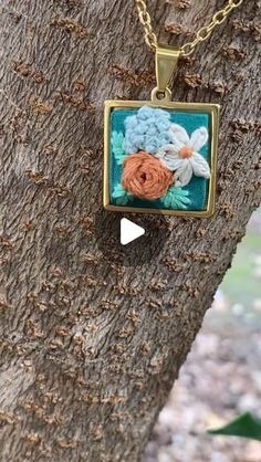 a square necklace with flowers on it hanging from a tree branch in front of the camera