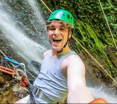 a young man wearing a green helmet is zipping through the water in front of a waterfall