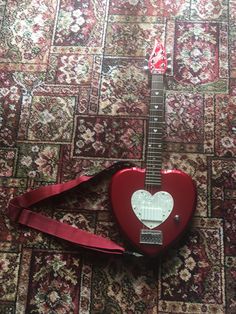 a red guitar laying on top of a carpet next to a bag with a heart on it