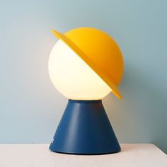 a yellow and blue lamp on top of a white table next to a blue wall