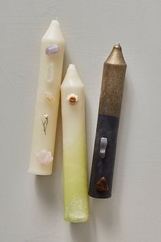 three different colored candles sitting next to each other on a white surface, one has a lighter in it