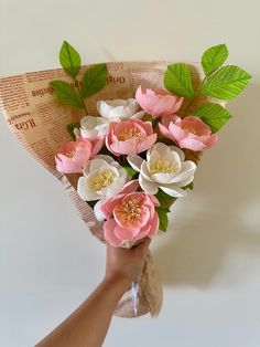 a hand holding a bouquet of pink and white flowers with green leaves on it's stems