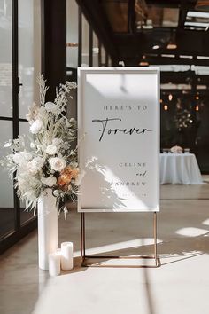 a sign that says here is to forever with flowers and candles in front of it